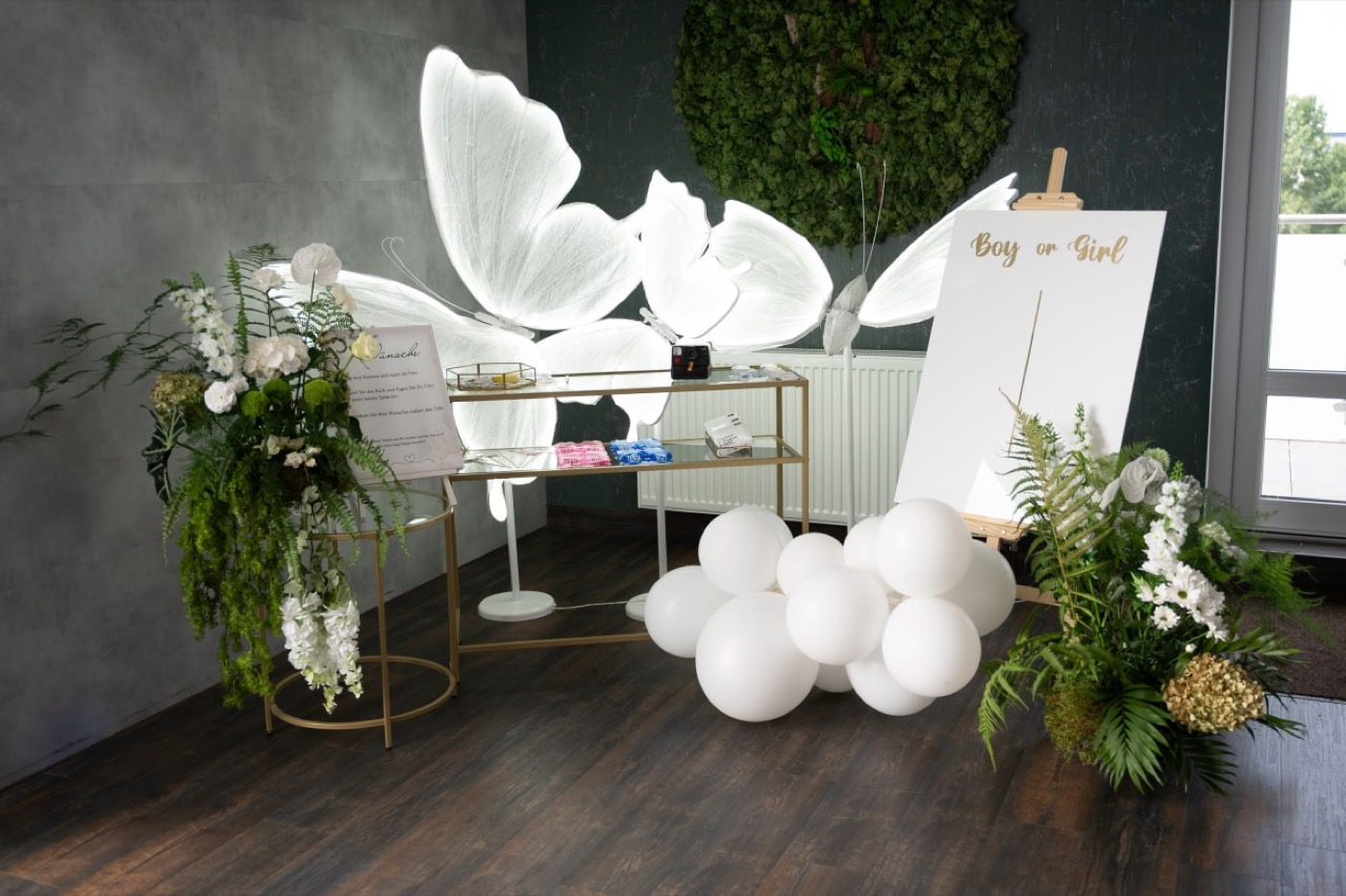 Gender Reveal Dekoration mit grünen Akzenten, weißen Ballons und Blumen.